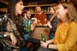A small group of best friends standing at a pub, drinking beer, chatting and having fun. Focus on bartender wiping drinking glass. Nightlife.