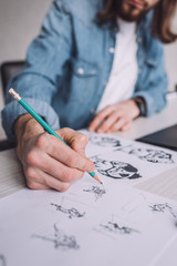 cropped view of illustrator drawing cartoon sketches on paper