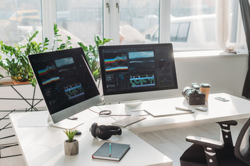 computer monitors with storyboard near headphones and paper cup on table