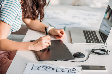cropped view of animator using digital tablet near sketches