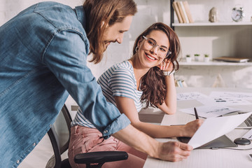 happy illustrator in glasses looking at coworker in studio