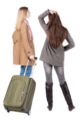 Wall Mural - Back view of two woman in winter jacket traveling with suitcas.