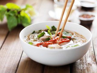 Wall Mural - eating a bowl of vietnamese beef pho with chopsticks and spicy sriracha sauce