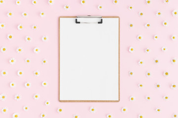 Top view of a wooden clipboard mockup with daisy decoration on a pink background.