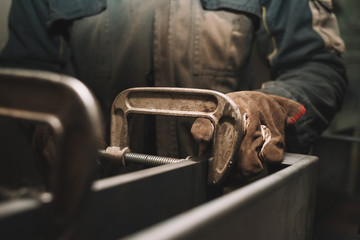 Man clamps iron products into c-clamps. Man works with clamps. Steel workshop concept