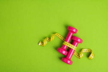 Fitness concept. Weight loss. Dumbbells and measuring tape on green mat background