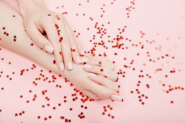 Wall Mural - Stylish trendy nail young woman hands pink manicure on background with red star confetti, top view. Concept skin care spa