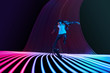 Caucasian young skateboarder riding on dark neon lighted line background. Training in action and motion on colorful waves. Concept of hobby, healthy lifestyle, youth, action, movement, modern style.