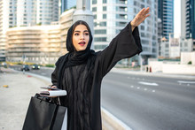 Beautiful Arab Woman In Abaya With Shopping Bags, Phone And Wallet Hitching A Taxi On The Street