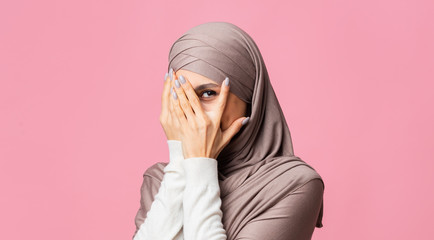 Wall Mural - Portrait of shy modest islamic girl in hijab peeking through fingers