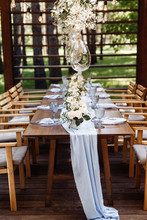 Festive Table. The Festive Table Is Decorated With Flowers, Greenery, Candles, A Blue Tablecloth, Crystal Plates, Glasses. Outdoors