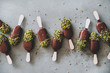 Ice cream popsicle pattern. Flat-lay of chocolate glazed ice cream pops with pistachio icing over grey concrete background, top view. Summer seasonal cold sweet healthy vegan dessert
