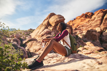 Wall Mural - female hiker sitting on edge of cliff at red rock canyon with bottle of water