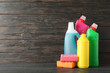 Bottles with detergent and sponges on wooden background, space for text