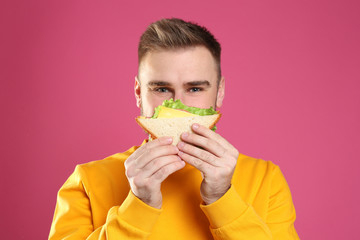 Wall Mural - Young man eating tasty sandwich on pink background