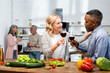 © LIGHTFIELD STUDIOS - selective focus of smiling woman and african american man talking and holding wine glasses, multicultural friends talking on background