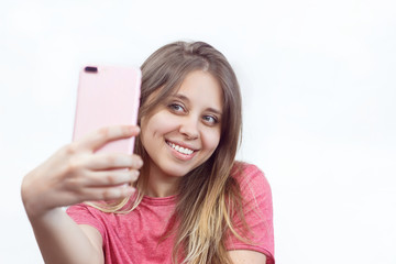 Wall Mural - Portrait of a caucasian happy smiling girl in a pink t-shirt who takes a selfie. Isolated white background. Real sincere emotions. Young woman with a beautiful smile. Even teeth of natural color