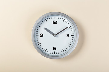 White wall clock with a yellow used hanging on the wall. Minimalist image of a wall clock on a beige background with copy space