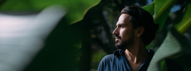 Conceptual portrait of a man in large banana leaves.