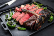 Barbecue dry aged wagyu porterhouse beef steak with large fillet piece sliced as closeup on a black modern design tray with green chili
