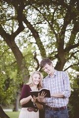 Canvas Print - Smiling couple reading the bible in a garden under sunlight with a blurry background