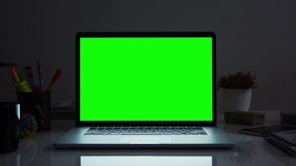 Laptop with green screen. Dark office. Dolly in. Perfect to put your own image or video. Track with perspective corner pin.   