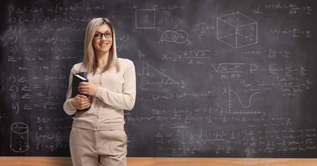 young female teacher in front of a school blackboard smiling