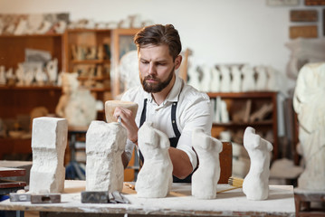 Wall Mural - Male craftsman in working uniform makes a limestone copy of woman torso at the creative studio and show making process from start to finish.