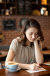 © Blue Jean Images - Elegant woman writing postcard in cafe