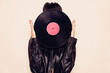 © Laura Barriuso/ADDICTIVE STOCK - Faceless woman in leather jacket hiding face behind vinyl record in studio on pink background