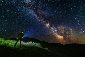 Wall Mural - bright starry sky with the milky way on the background of mountains and hiker with red tent.
