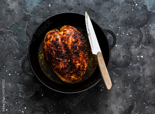Fotografía Simple baked chicken breast in a cast iron pan on a dark background, top view