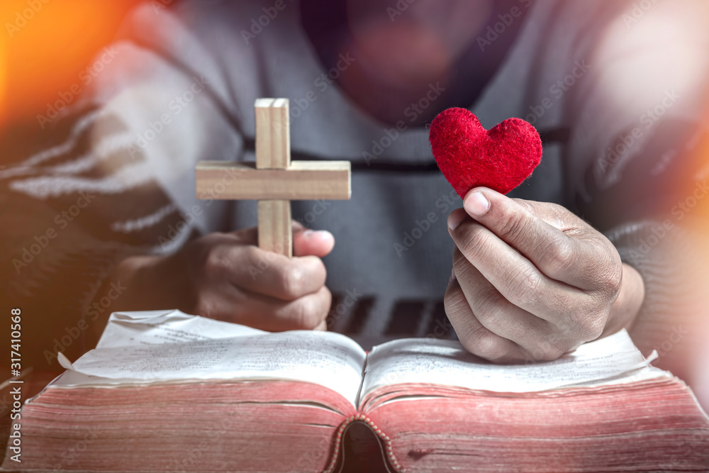 Man holding a red heart in hand with Cross on Bible with light in ...