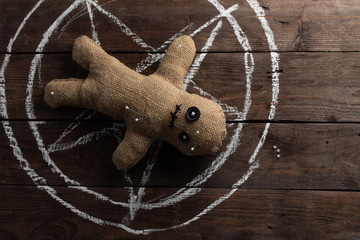 Voodoo doll on a wooden background with dramatic lighting. The concept of witchcraft and black art and the occult. Burlap doll on the background of a drawn star. Stuck pins in the doll.