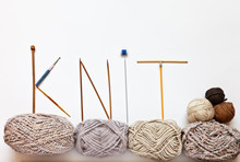 The Word "knit" Is Written With Knitting Needles And Hooks On Balls Of Woolen Yarn On A White Background. Hand Knitting And Craft Concept. Free Space For Text, Flat Lay
