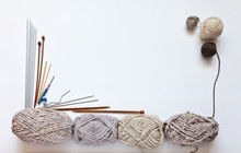 Balls Of Wool Yarn In Beige Shades And Different Types Of Knitting Needles On A White Background. Hand Knitting And Hobby Concept. Free Space For Text, Flat Lay, Focus On Clews
