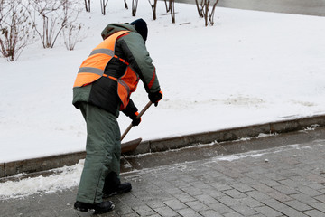 Wall Mural - Snow removal in winter, communal services worker in uniform with a shovel clears snow on a street