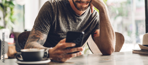 Fotografía Handsome bearded hipster man use smartphone with coffee at table in cafe