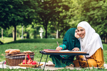 Wall Mural - Portrait of happy muslim mother and little muslim girls child learning together with hijab dress smiling and enjoy relax reading and write a book in summer park.Education concept