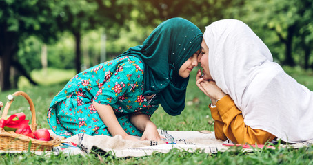 Wall Mural - Portrait of happy lovely family arabic muslim mother and little muslim girls child with hijab dress smiling and having fun hugging and kissing together in summer park