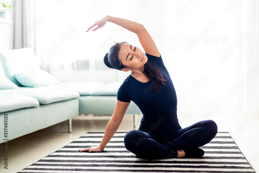 Young asian girl exercising at home on carpet in living room - obrazy, fototapety, plakaty 