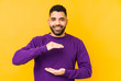 © Asier - Young mixed race arabic man isolated holding something with both hands, product presentation.