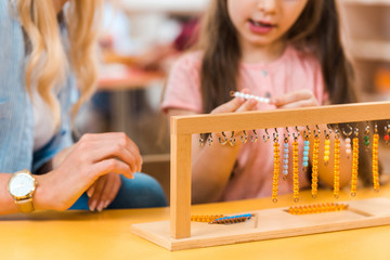 Selective focus of kid playing wooden game by teacher in montessori school, cropped view