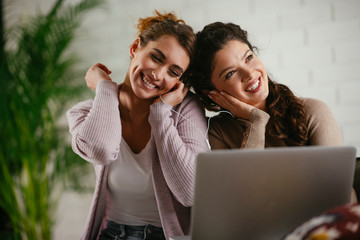 Two friend sitting on couch with laptop and listening music. Sisters having fun. 