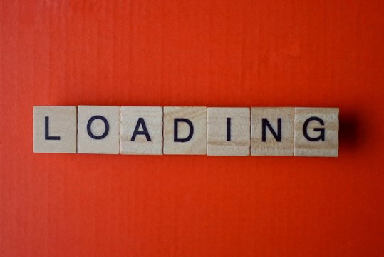 word loading from small gray wooden letters lies on a red background