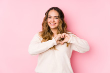 Young Curvy Woman Posing In A Pink Background Isolated Smiling And Showing A Heart Shape With Hands.