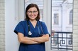 © Valerii Honcharuk - Smiling adult woman doctor in blue uniform stethoscope with folded arms, confident female medic looking at camera, standing near the window in clinic