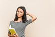 © Asier - Young asian woman student holding a book touching back of head, thinking and making a choice.