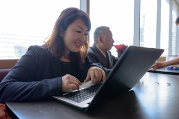 Wall Mural - Mature Asian businessman and mature Asian businesswoman using laptop at restaurant together