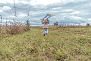 Little boy 3-5 years old, happy smile launches a kite in park, feel happy. Casual warm clothes with hood. Autumn day. Free space for copying text. Emotions of happiness and pleasure.